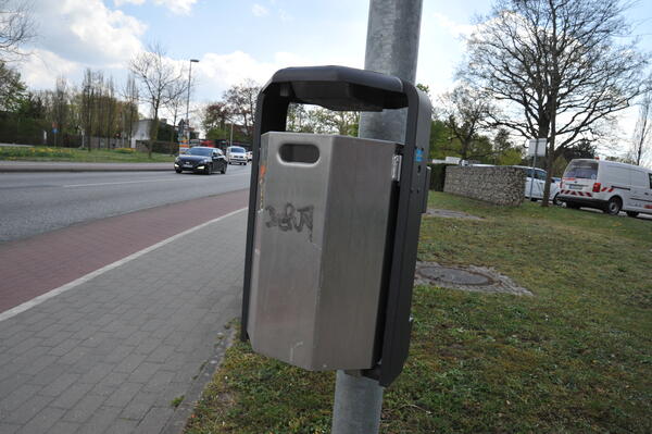 Ein Metallm&uuml;lleimer h&auml;ngt neben einer befahrenen Stra&szlig;e.