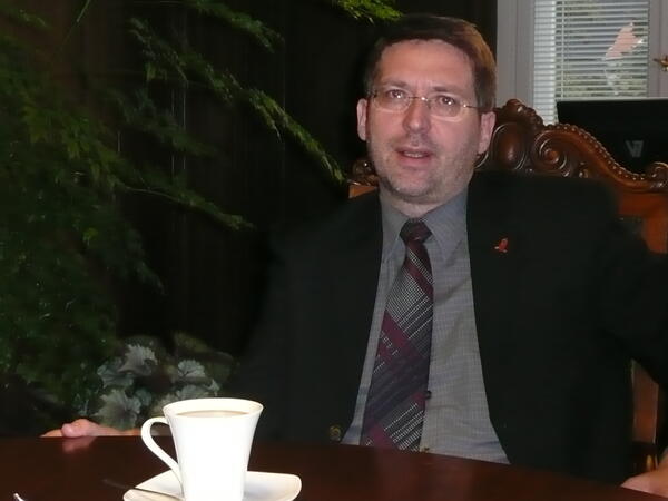 Dr. Oliver Hermann sitzt im Anzug an einem Tisch.