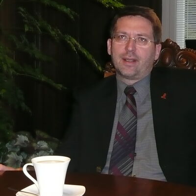 Dr. Oliver Hermann sitzt im Anzug an einem Tisch.