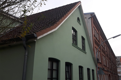 Grüne Hausfront mit giebelständigem Spitzdach.