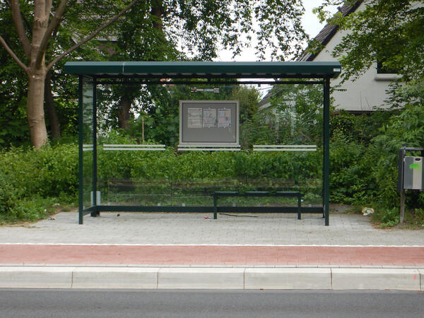 Eine leere Bushaltestelle vor einer grünen Hecke.