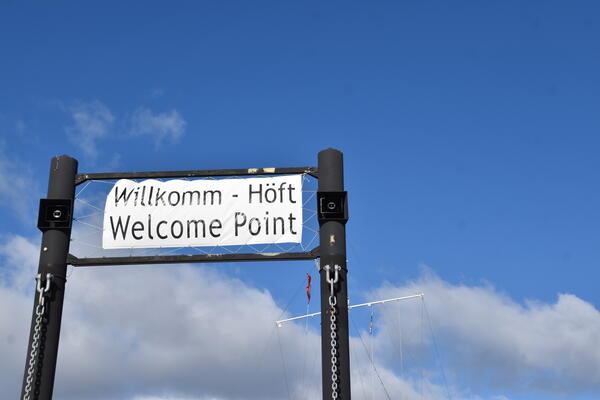 Das Schild am Steg ist zweisprachig und zeigt auch die englische Übersetzung: Welcome Point.