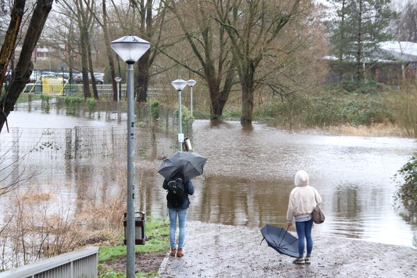 Zwei Passantinnen stehen mit Regenschirm vor einem überfluteten Gehweg im Krückaupark.