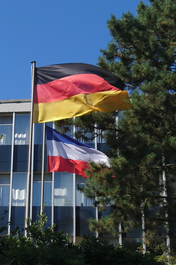 Wehende Flaggen vollmast vor dem Elmshorner Rathaus. Zu sehen sind die Bundesflagge und die Landesflagge Schleswig-Holstein.