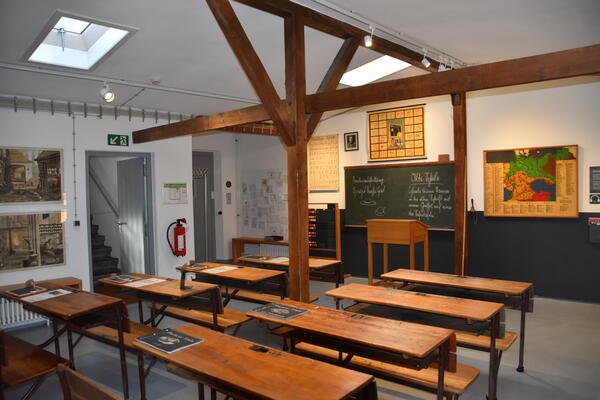 Altes Klassenzimmer mit Pults aus Holz und einer Kreidetafel mit altdeutscher Schrift.