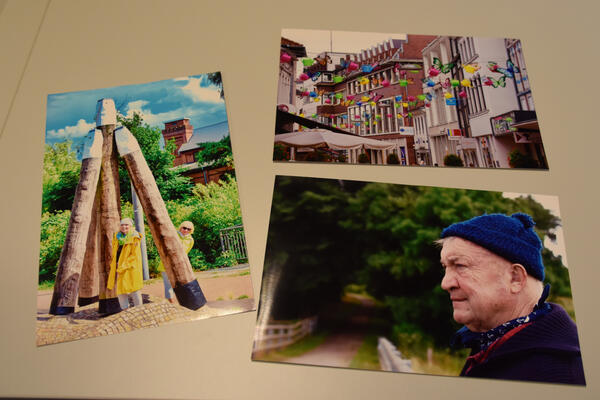 Bild vergr&ouml;&szlig;ern: Drei Fotos mit ganz unterschiedlichen Motiven liegen auf einem Tisch.Das Siegerfoto zeigt zwei in Gelb gekleidete Damen an dem Kunstwerk Sturmdalben.